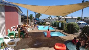 Un área de piscina con varias piscinas, sillas de descanso y una zona con sombra.