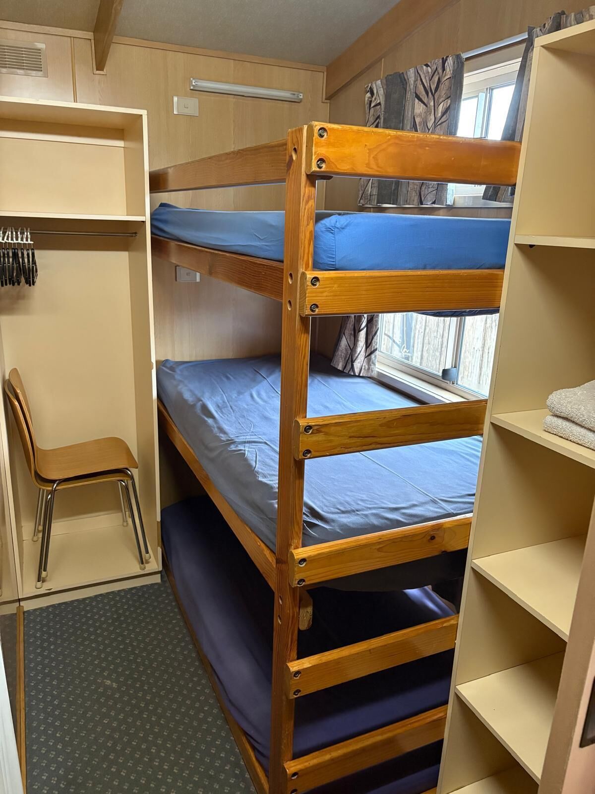 A bunk bed with a desk and chair, a window with curtains, and a shelf with towels.