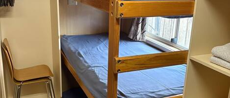 A bunk bed with a desk and chair, a window with curtains, and a shelf with towels.