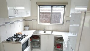 Cocina compacta con armarios blancos, estufa a gas, horno empotrado, pileta y refrigerador.