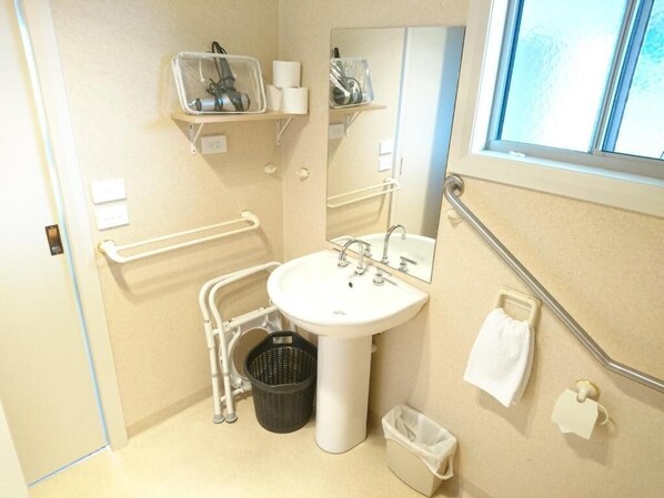 A small bathroom with a sink, mirror, and handrails. There are shelves above the sink holding toiletries.