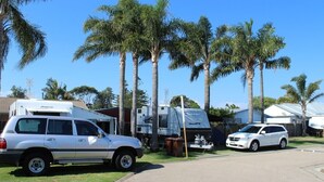 Un camping con vehículos recreativos, una camioneta SUV blanca y una minivan blanca estacionados sobre césped.