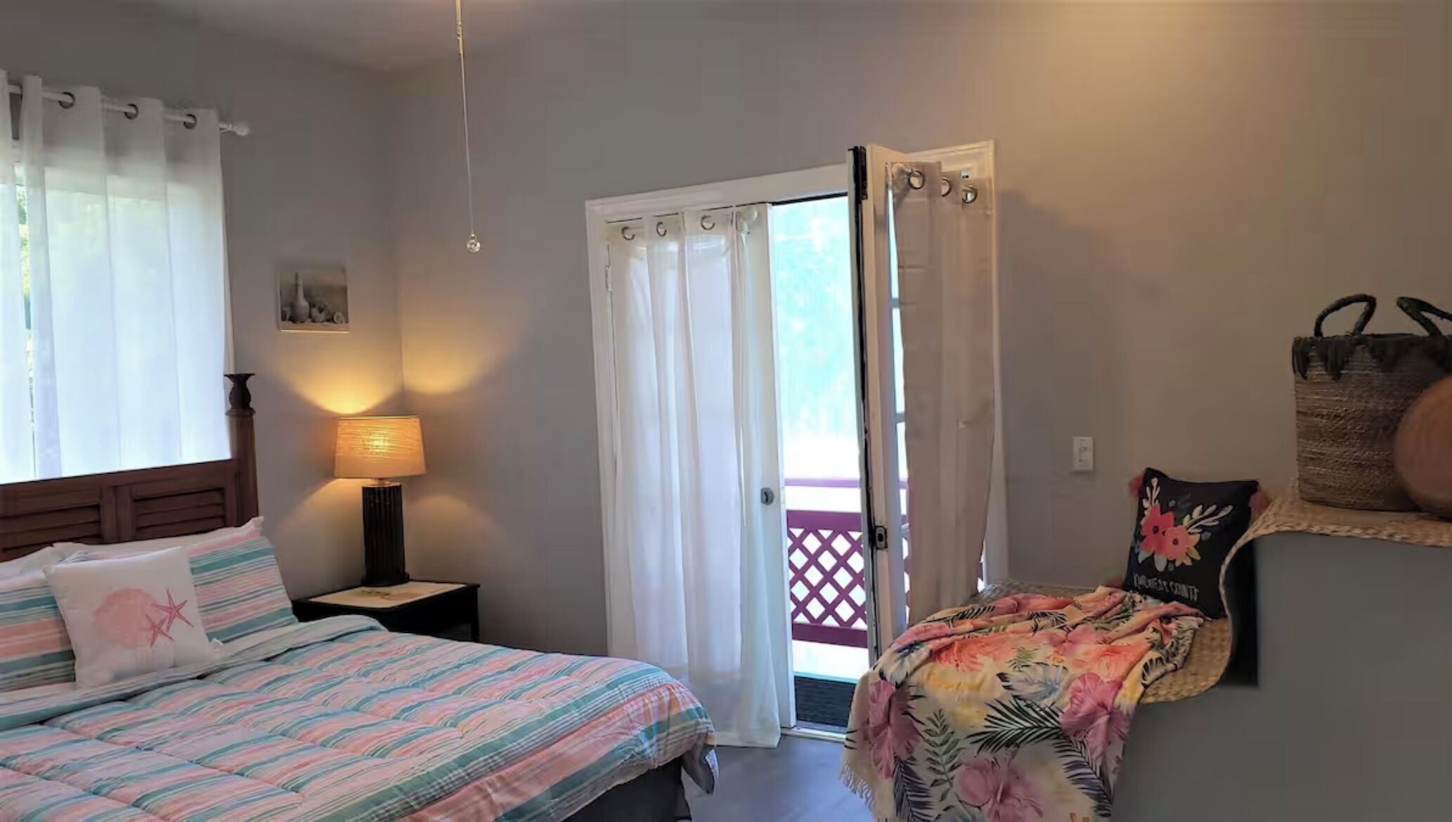 A bedroom with a bed, a nightstand, a lamp, a door leading to a balcony, and a wall-mounted basket.