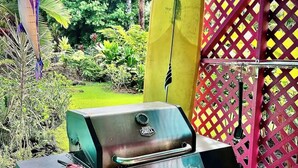 Een buitenbarbecue met een groen-zwart kleurenschema, omringd door een kleurrijke lattenheining en een surfplank.