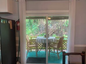 A room with a sliding glass door leading to an outdoor deck with a table and chairs. - The Famous Peacock House (Pāhoa)