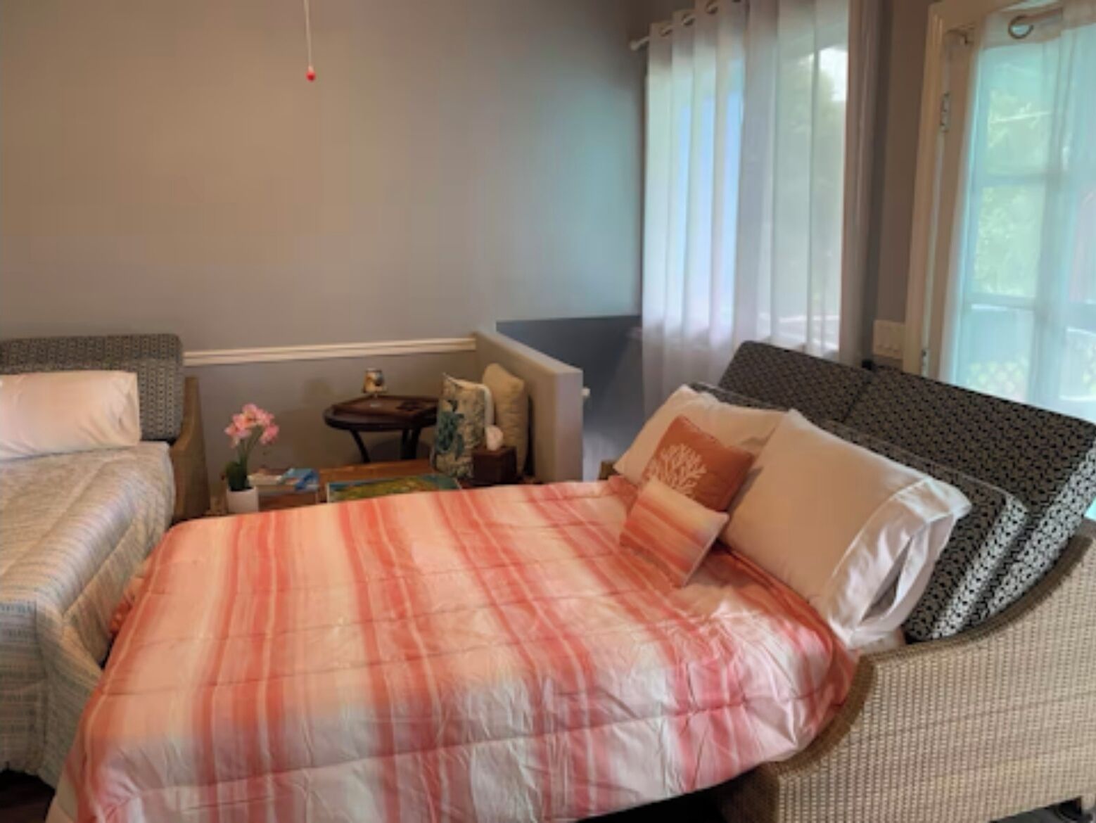 A hotel room with a large bed, a smaller bed, a nightstand, a small table, and a window with curtains.