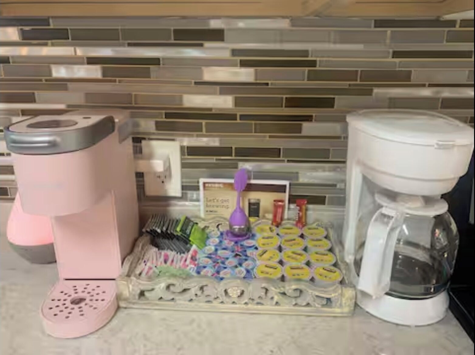 Una cocina con cafetera, tetera y bandeja de bolsitas de té.
