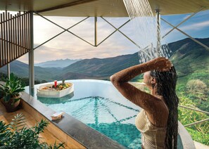 A person enjoying a shower in a infinity pool with a mountain view. - Monticle Glamp (Peermade)
