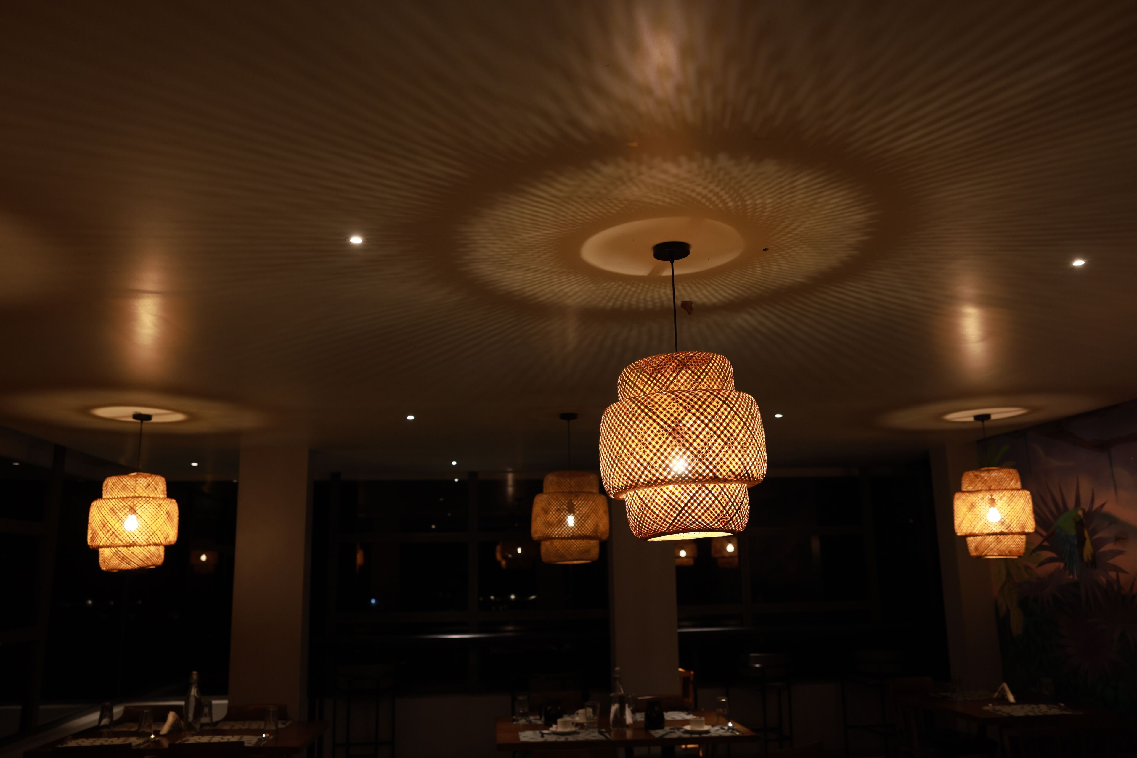 Interior de restaurante con poca luz, varios candelabros colgantes de mimbre y un elemento decorativo central en el techo.