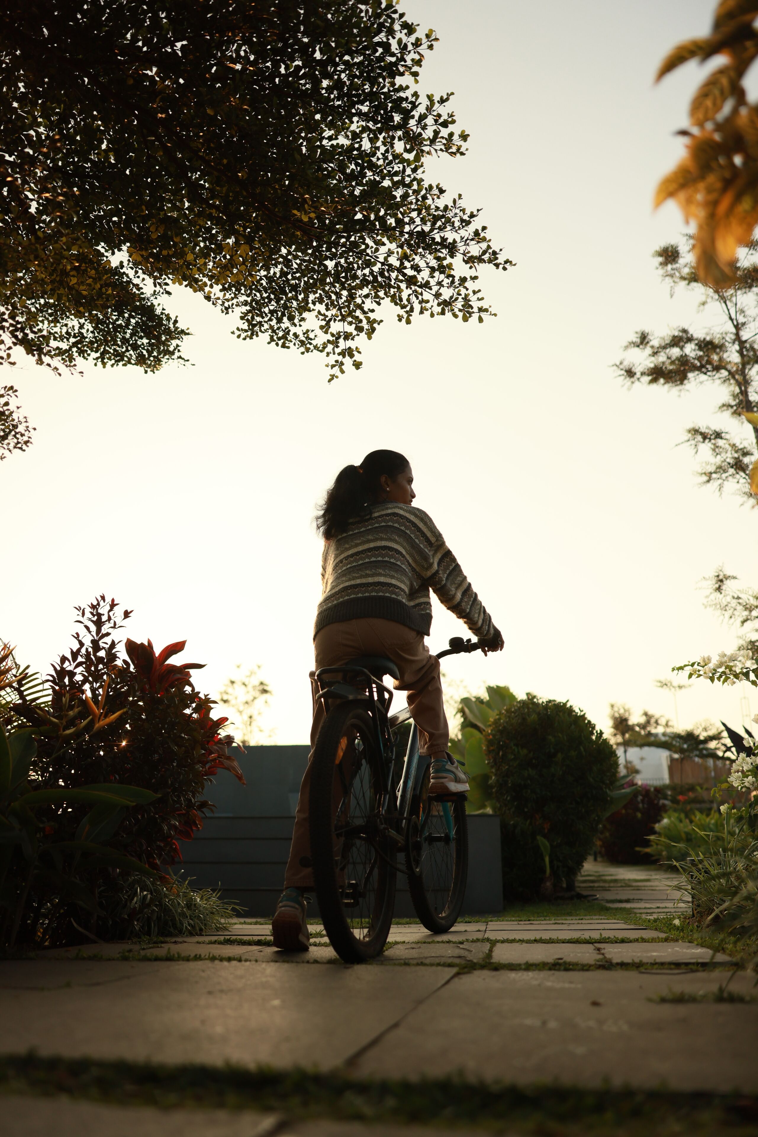 A person riding a bicycle on a pathway with greenery and a building in the background.