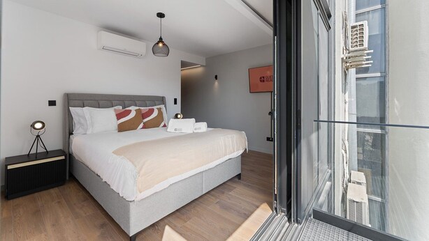 A modern bedroom with a bed, bedside table, and a view of the city through a large window. - GuestReady - Age of Discoveries - Gama (Porto)