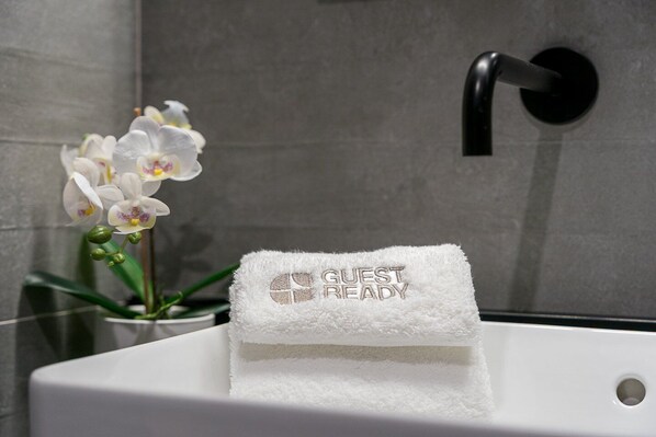 Un baño con un lavamanos blanco, una toalla bordada con la leyenda 'GUEST READY' y una planta de orquídea.