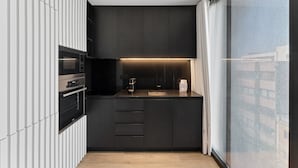 A modern kitchen with dark cabinetry, a built-in oven, a coffee machine, and a window with a view. - GuestReady - Age of Discoveries - Cabral Apt (Porto)