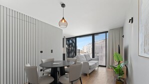 A modern living room with a round table, grey sofas, and a large window offering a city view. - GuestReady - Age of Discoveries - Cabral Apt (Porto)
