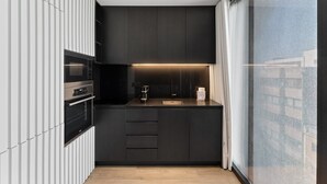 Une cuisine moderne avec des meubles de couleur sombre, un four encastré, une machine à café et une fenêtre offrant une belle vue.