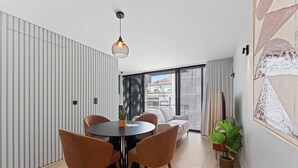 Un espace repas moderne avec une table ronde, quatre chaises, un luminaire suspendu et une vue sur la ville grâce à de grandes fenêtres.