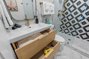 Een badkamer met een witte wastafel, een spiegel, een toilet en een douche.