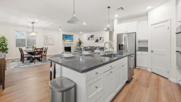 A modern kitchen with white cabinets, granite countertops, stainless steel appliances, and pendant lighting.