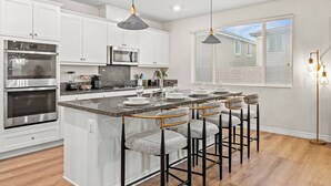 A modern kitchen with white cabinets, stainless steel appliances, a granite countertop, and bar stools.