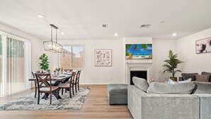 A modern living room with a grey sofa, dining table with chairs, and a fireplace.