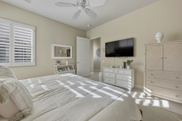 A bedroom with a bed, a television, a dresser, and a ceiling fan.
