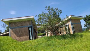 A two-story building with brick walls and a flat roof, surrounded by lush greenery and trees. - Cabañas Entrada a la Sierra (Zacapoaxtla)