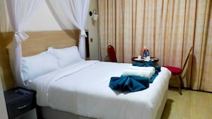 A hotel room with a bed, a nightstand, a chair, a table with a water bottle, and a curtain. - Ack Guest House Machakos (Machakos)