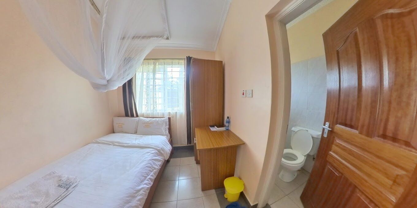 A small, compact bedroom with a bed, bedside table, and a toilet.
