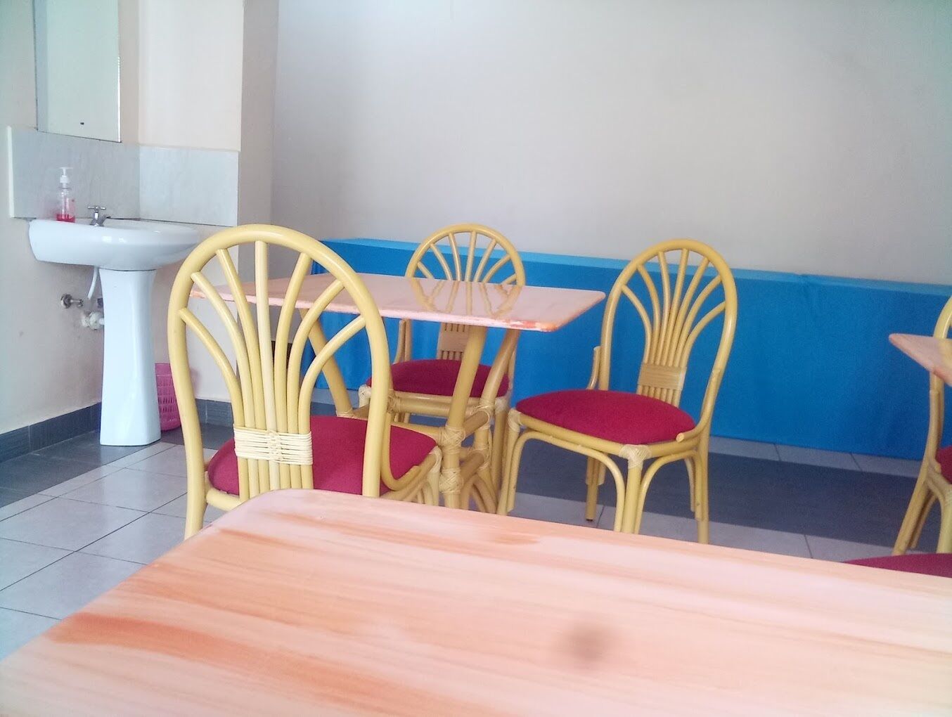 A dining area with a white sink, yellow wicker chairs with red cushions, and a wooden table.