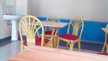 Un comedor con un lavamanos blanco, sillas de mimbre amarillas con cojines rojos, y una mesa de madera.