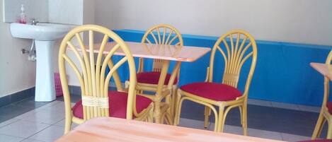 A dining area with a white sink, yellow wicker chairs with red cushions, and a wooden table.
