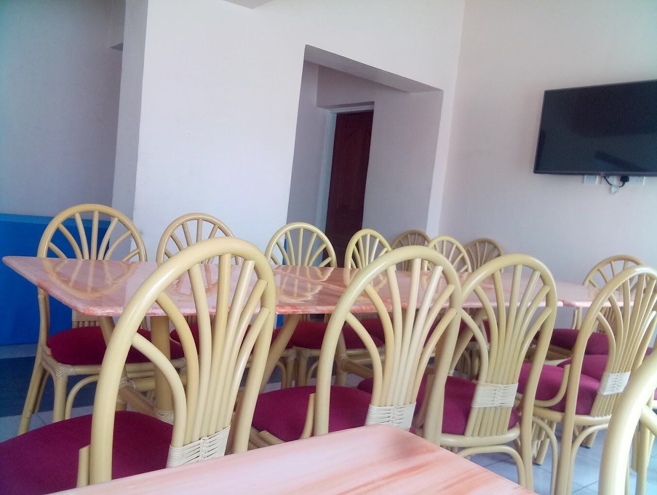 A dining area with multiple tables and chairs, a television mounted on the wall, and a door leading to another room.