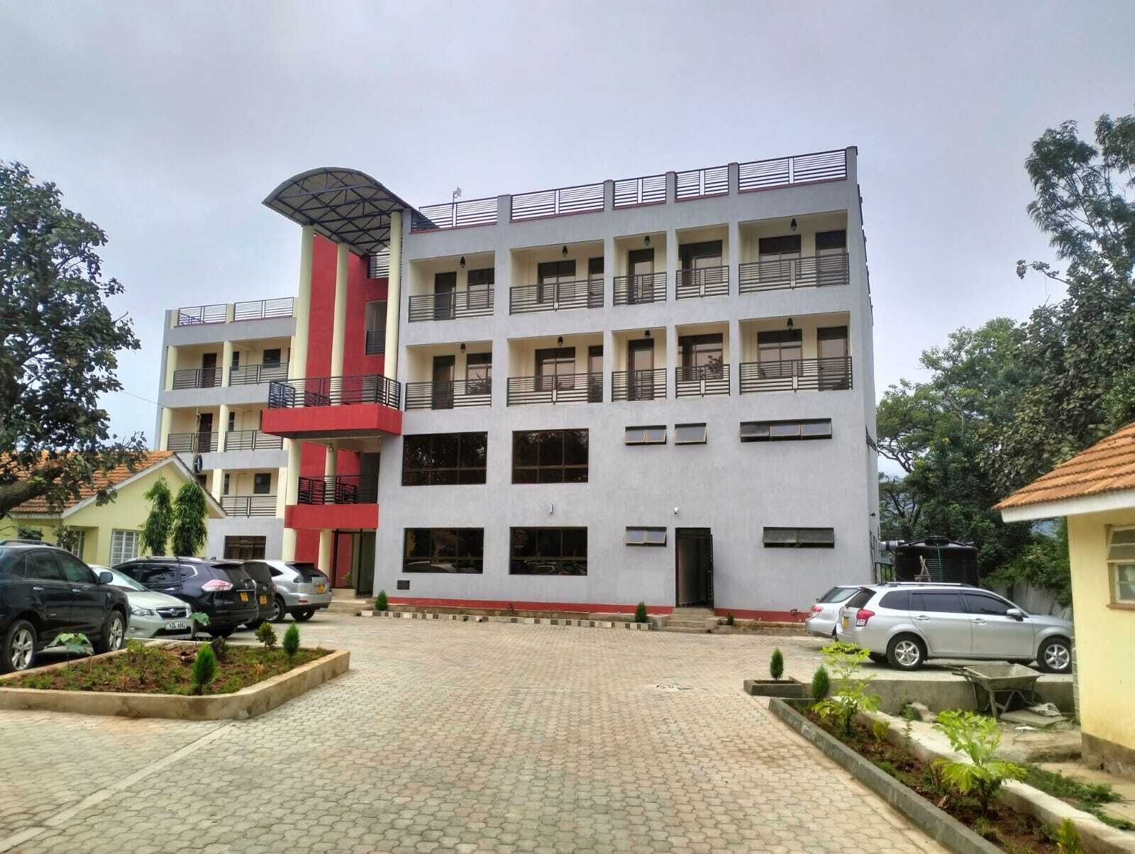 A multi-story building with a flat roof, a central red vertical structure, and a covered entrance.