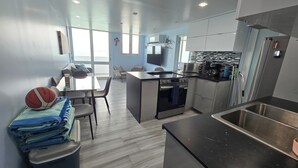 Eine moderne Küche mit Edelstahlgeräten, ein Essbereich mit Tisch und Stühlen sowie ein Blick ins Freie durch große Fenster.
