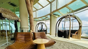 Un intérieur moderne avec un grand plafond en verre, des canapés en cuir, une table ronde en bois et une vue sur les gratte-ciel de la ville.
