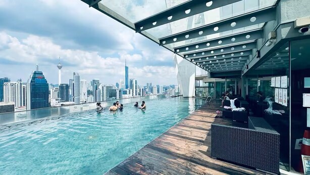 Une piscine à débordement située sur le toit, offrant une vue panoramique sur la ville, avec une terrasse en bois et des espaces de détente.
