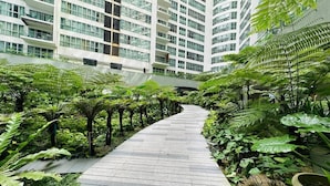 Un chemin bordé d’une végétation luxuriante et de bâtiments modernes de grande hauteur.