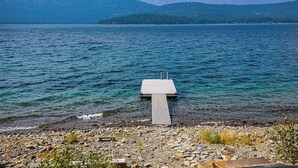 A wooden dock extending into a calm lake with a rocky shoreline and distant mountains. - Lakefront Home. Built 2016. For Remote work, boating, relaxing, hiking. (Marion)