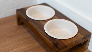A wooden pet feeding station with two white bowls on a wooden floor.