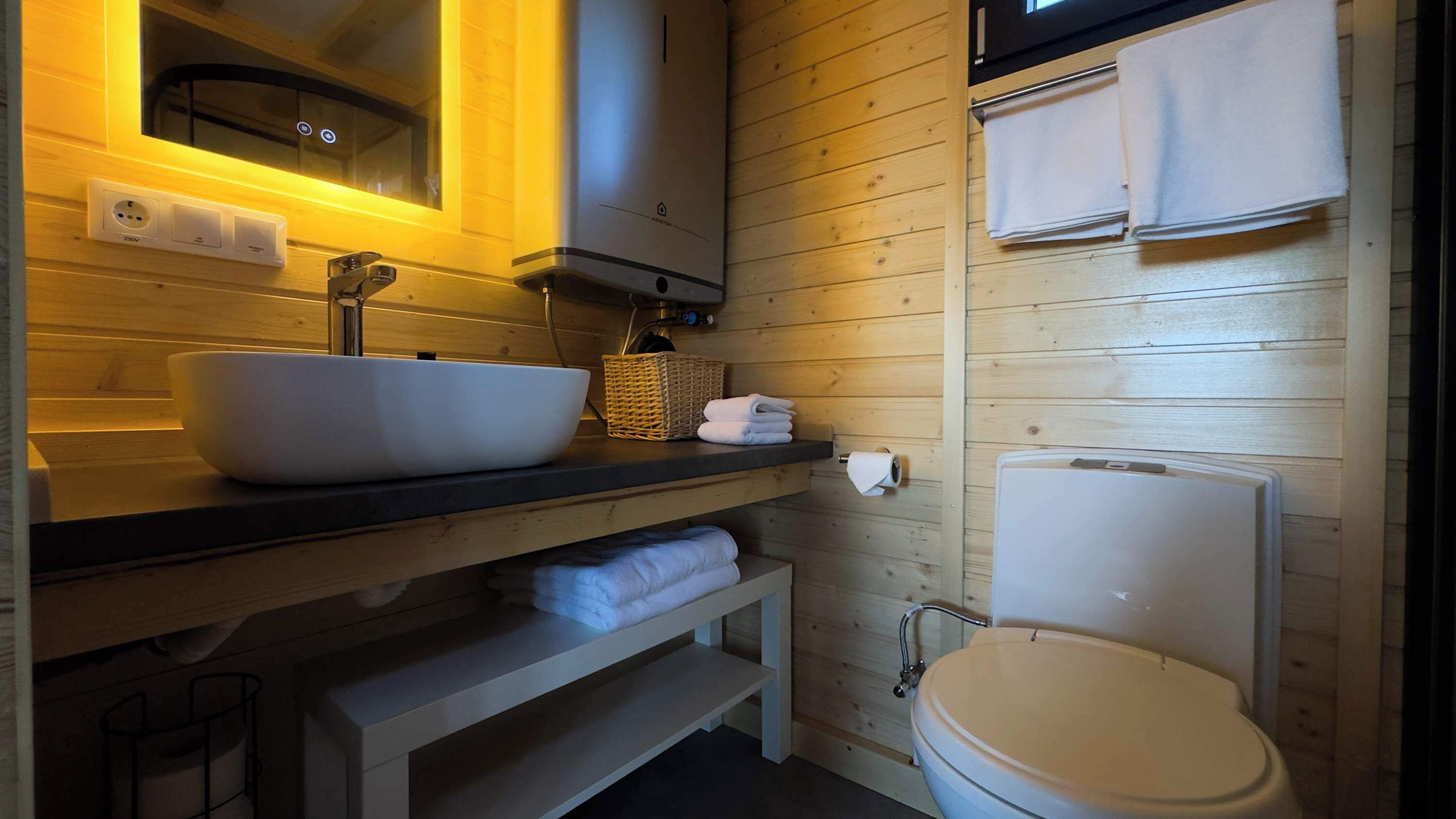 Un baño estilo cabaña de madera con un lavabo blanco grande, un inodoro, un espejo y un estante con toallas.