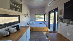 Una habitación compacta y moderna con cama, kitchenette y ventanas amplias.
