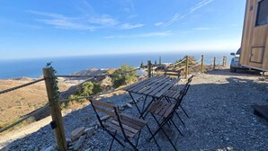 Mesa y sillas de madera sobre un camino de grava con una barrera de cuerda, con vistas a un paisaje costero.