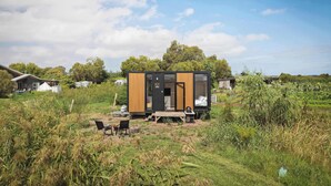 A modern, compact cabin with a wooden exterior, a small porch, and a visible bedroom.
