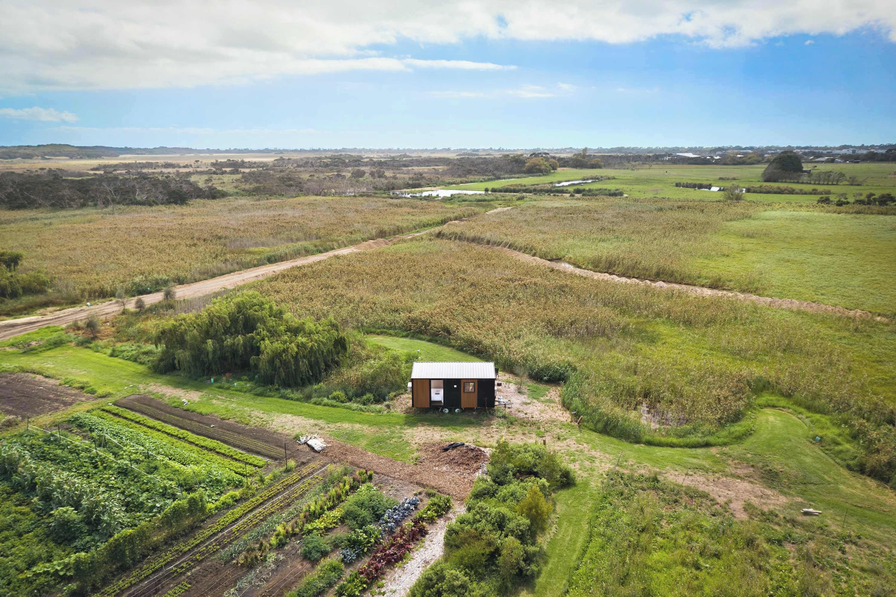 Paisaje rural con una construcción pequeña rodeada de campos y un sendero de tierra.