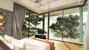 A modern bedroom with a large bed, a ceiling fan, and a view of trees through floor-to-ceiling windows.