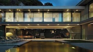 A modern house with a swimming pool, large windows, and a staircase leading to the upper floor.