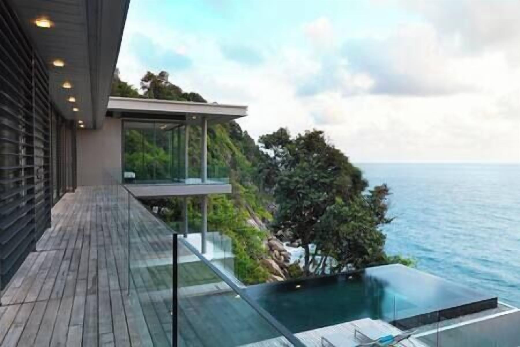 Una piscina infinita moderna al aire libre con vistas al mar, una terraza de madera y una barandilla de cristal.