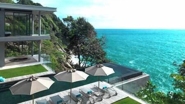 A modern villa with a glass balcony overlooking a clear blue sea.