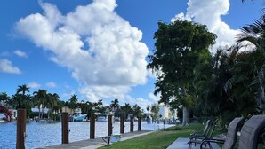 A waterfront patio with chairs and a concrete walkway. - Relax & Unwind – Walk to the Beach from This 2BR -2BA with Pool and fishing dock (Pompano Beach)