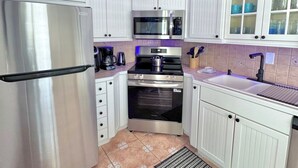 A modern kitchen with white cabinetry, stainless steel appliances, and a tiled backsplash. - Relax & Unwind – Walk to the Beach from This 2BR -2BA with Pool and fishing dock (Pompano Beach)